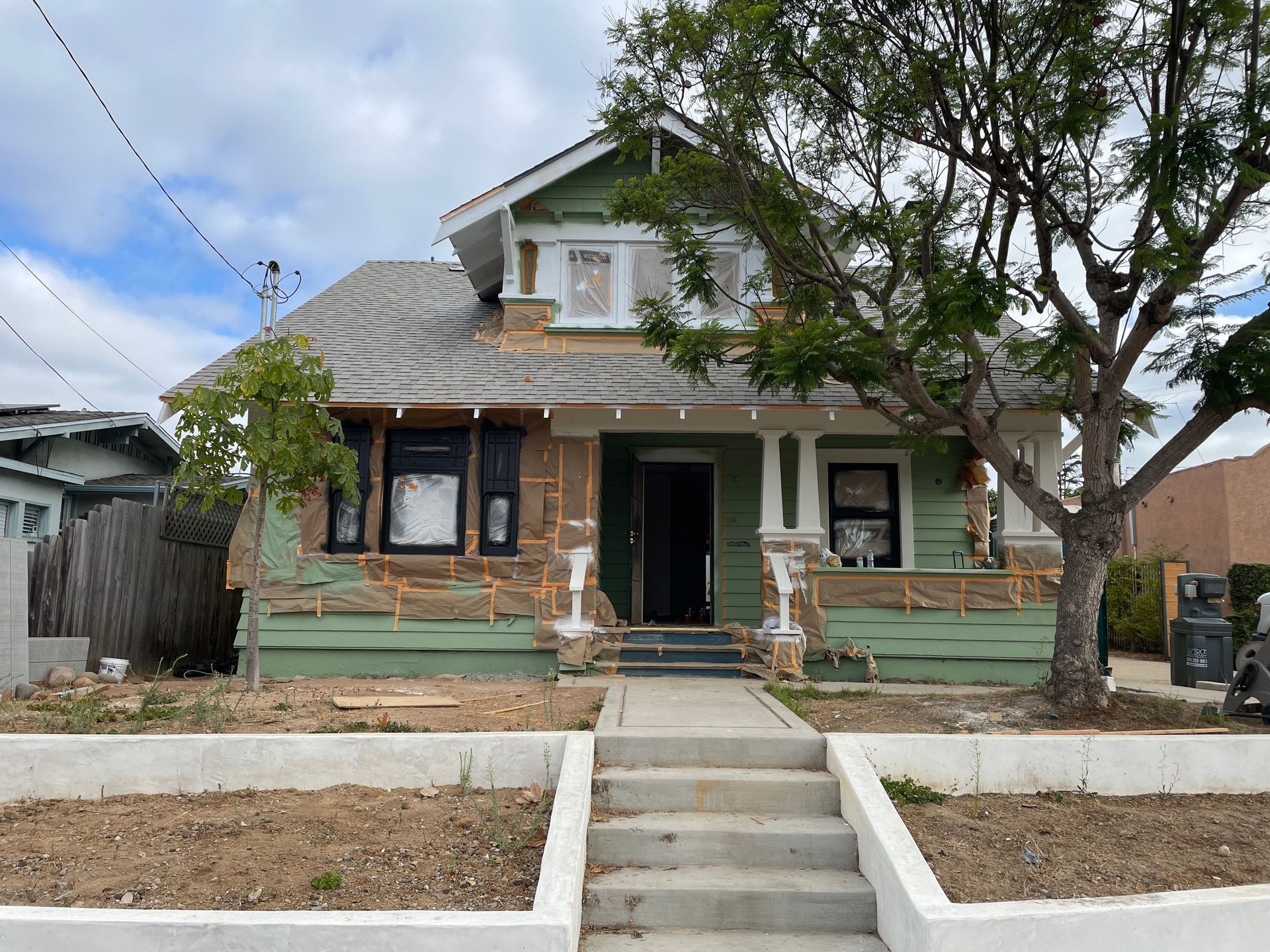 House exterior under renovation with exposed insulation. Green siding, gray roof, concrete steps.