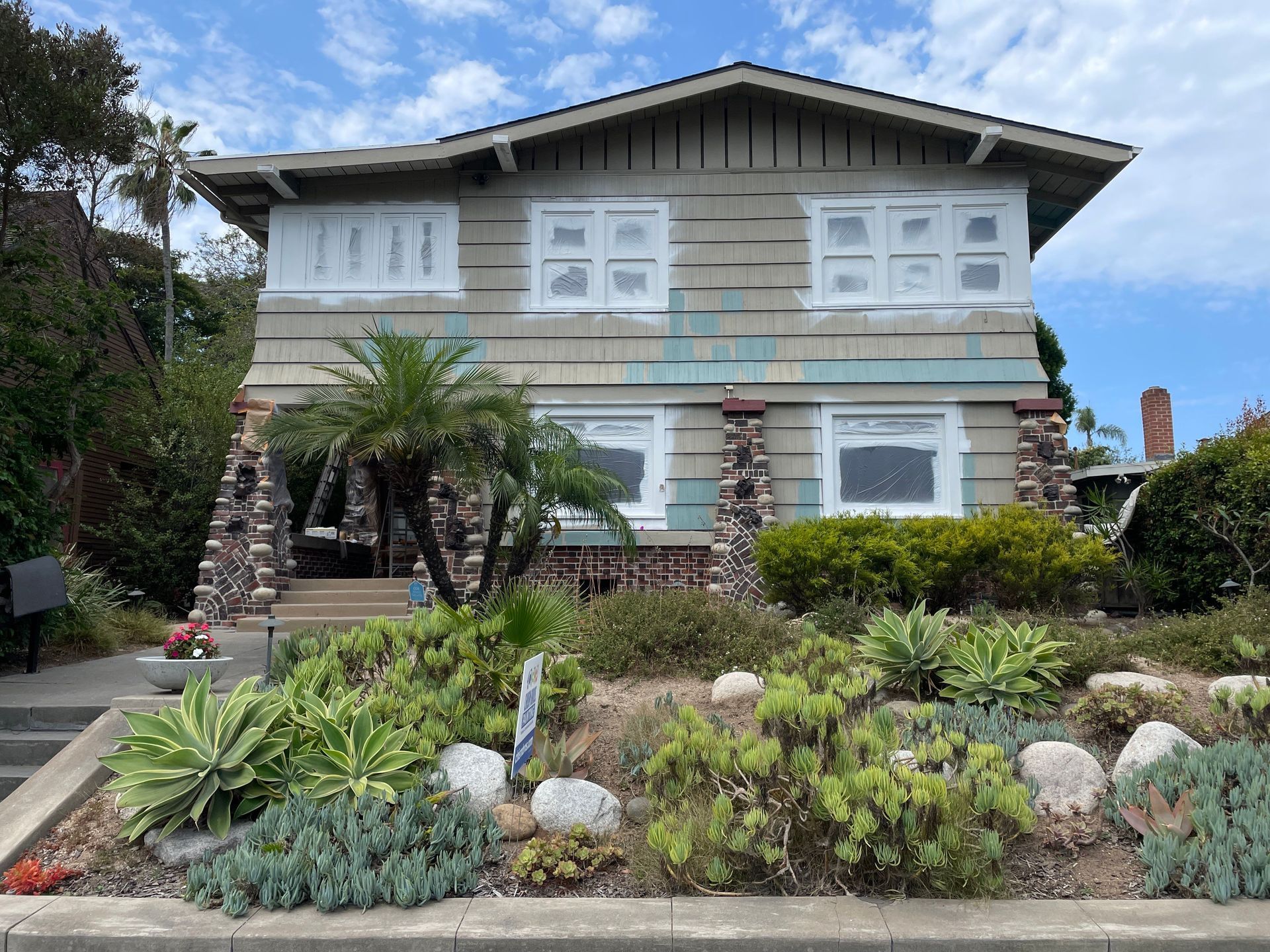 Two-story house with beige siding, window coverings, and a lush garden in front.