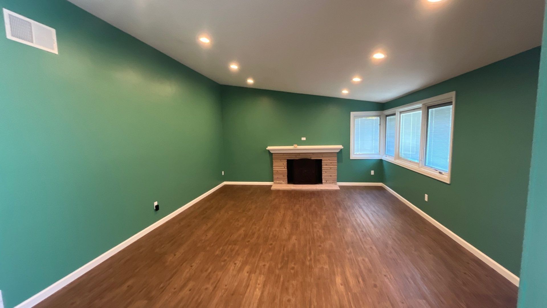 Green-walled living room with a fireplace, hardwood floors, and recessed lighting.