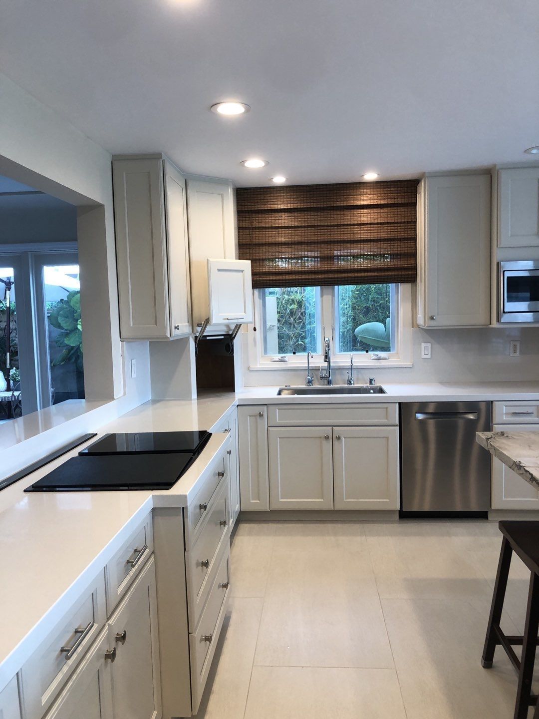 Bright kitchen with white cabinets, stainless steel appliances, and a woven window shade.
