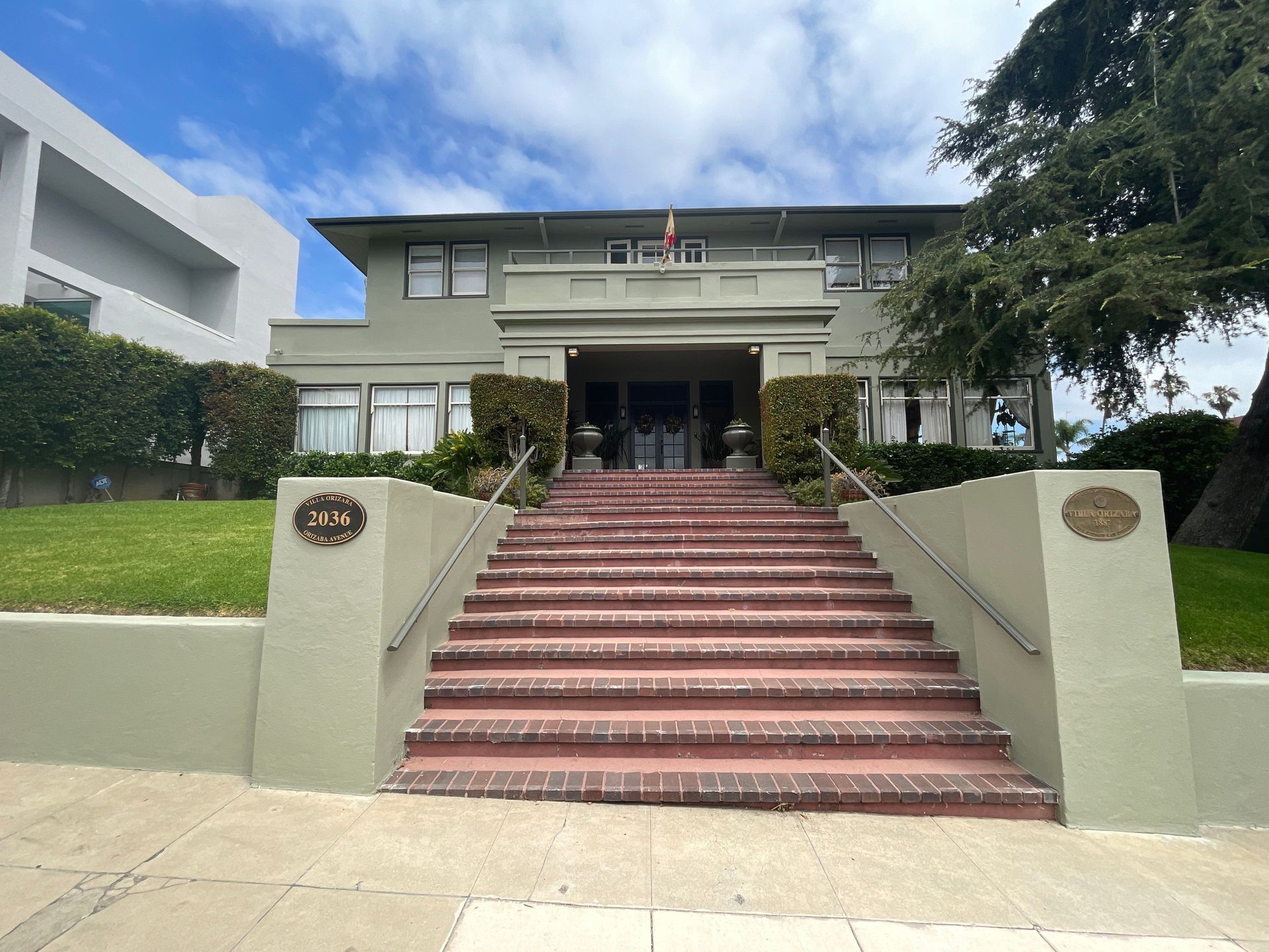 Two-story light green building with red brick stairs. Address plaque visible.