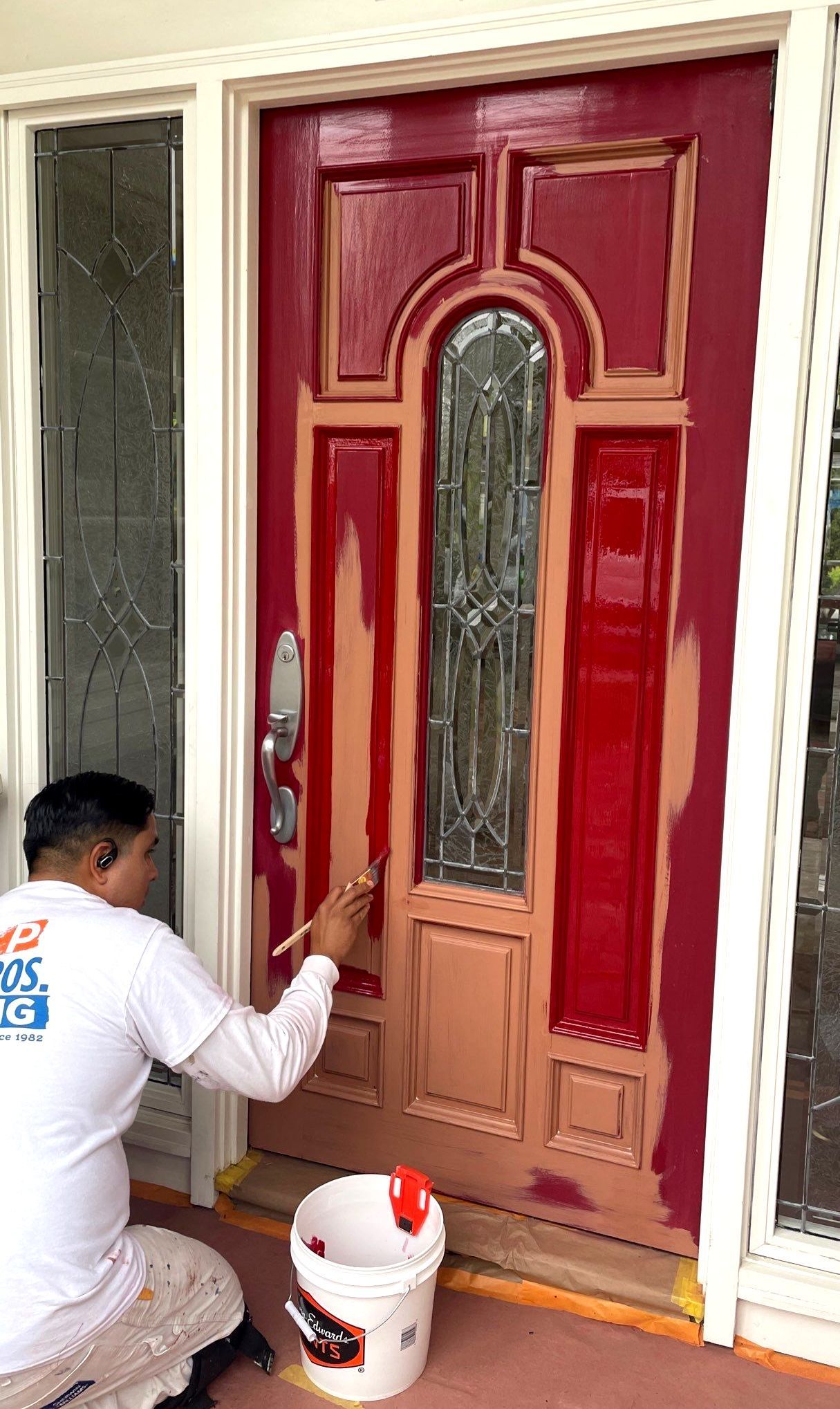 Person painting a red front door, using a paintbrush and bucket, outdoors.