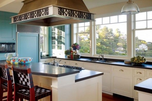 Kitchen with blue cabinets, stainless steel range hood, and large windows overlooking trees.