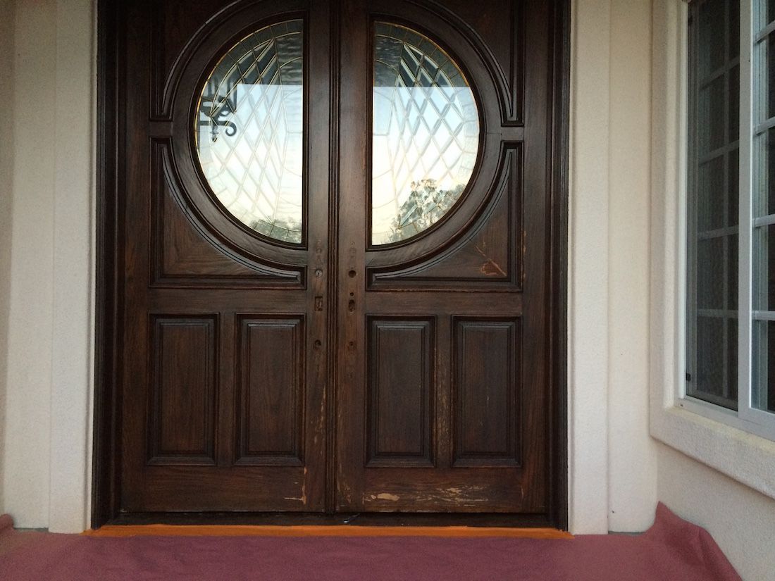 Dark wooden double doors with round glass windows, framed by white trim.