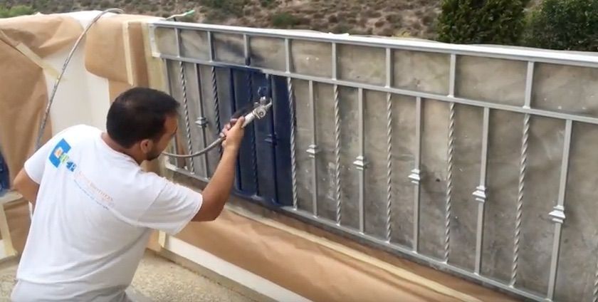 Man spray painting a metal railing blue outdoors, wearing a white shirt.