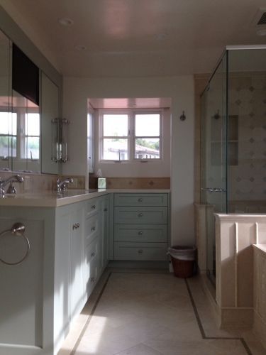 Bathroom with blue cabinets, window, glass shower, and light beige floor.