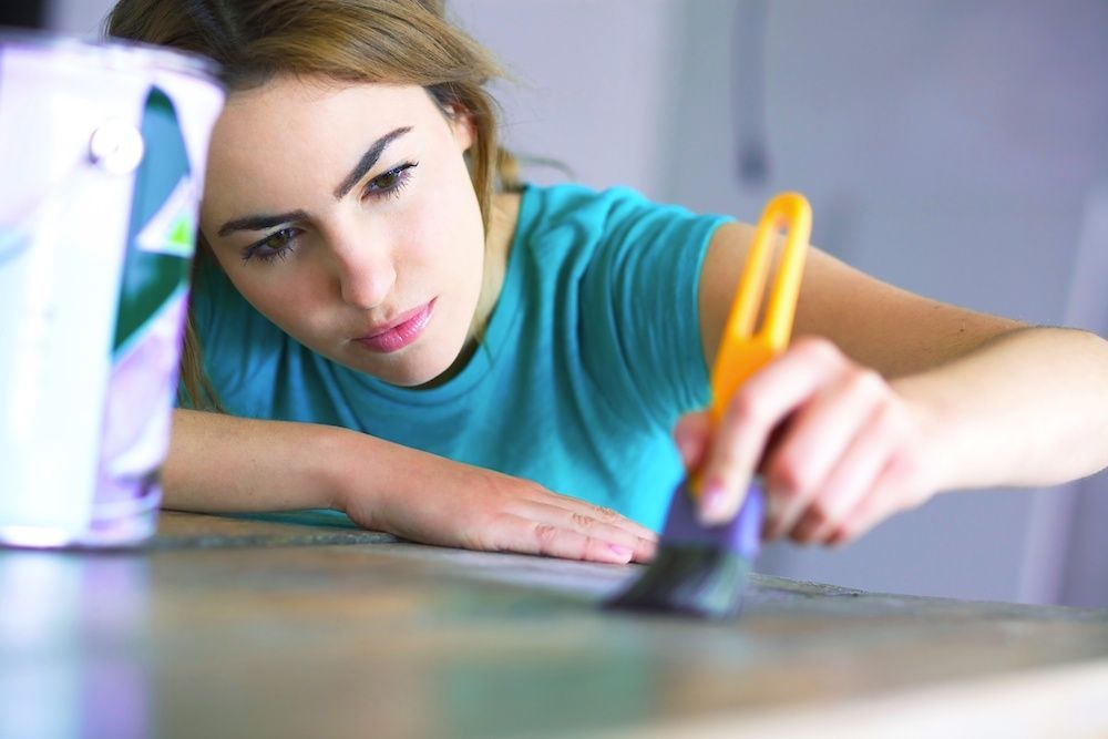 Woman painting wood surface with brush; holding brush; looking intently.