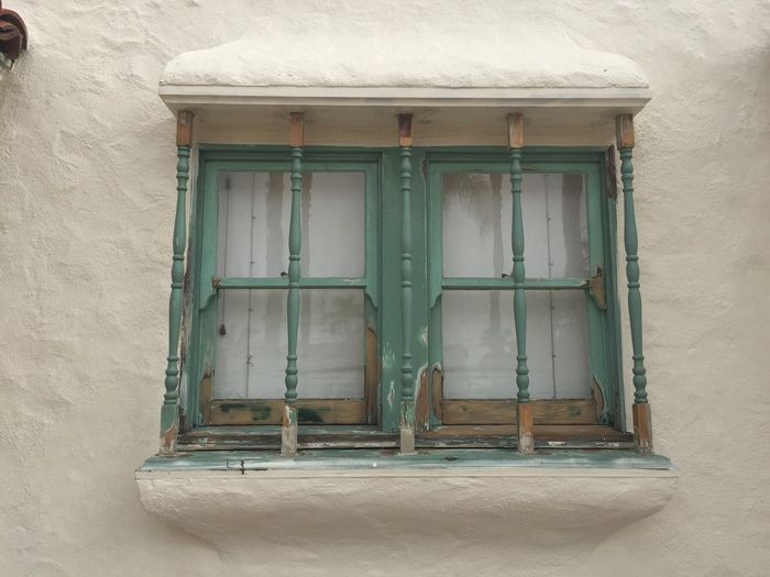 Green-framed window with vertical bars, set in a white stucco wall.