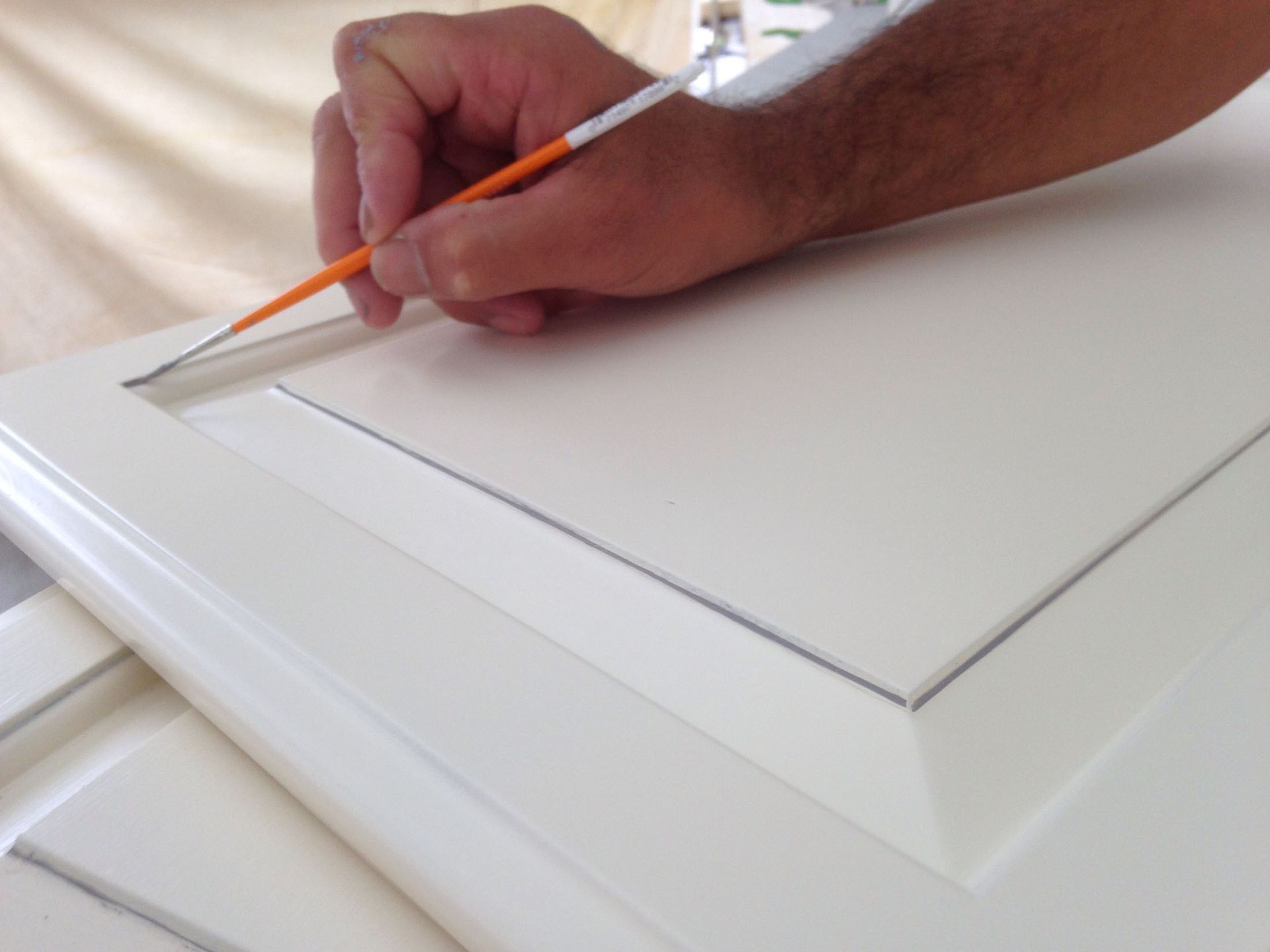 Hand painting a white cabinet door with an orange-handled brush.