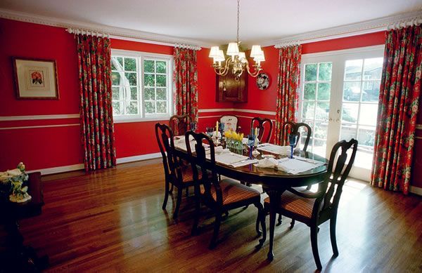 Red dining room with oval table set for a meal, floral curtains, and a chandelier.