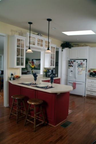 Red kitchen island with stools, white cabinets, and pendant lights.