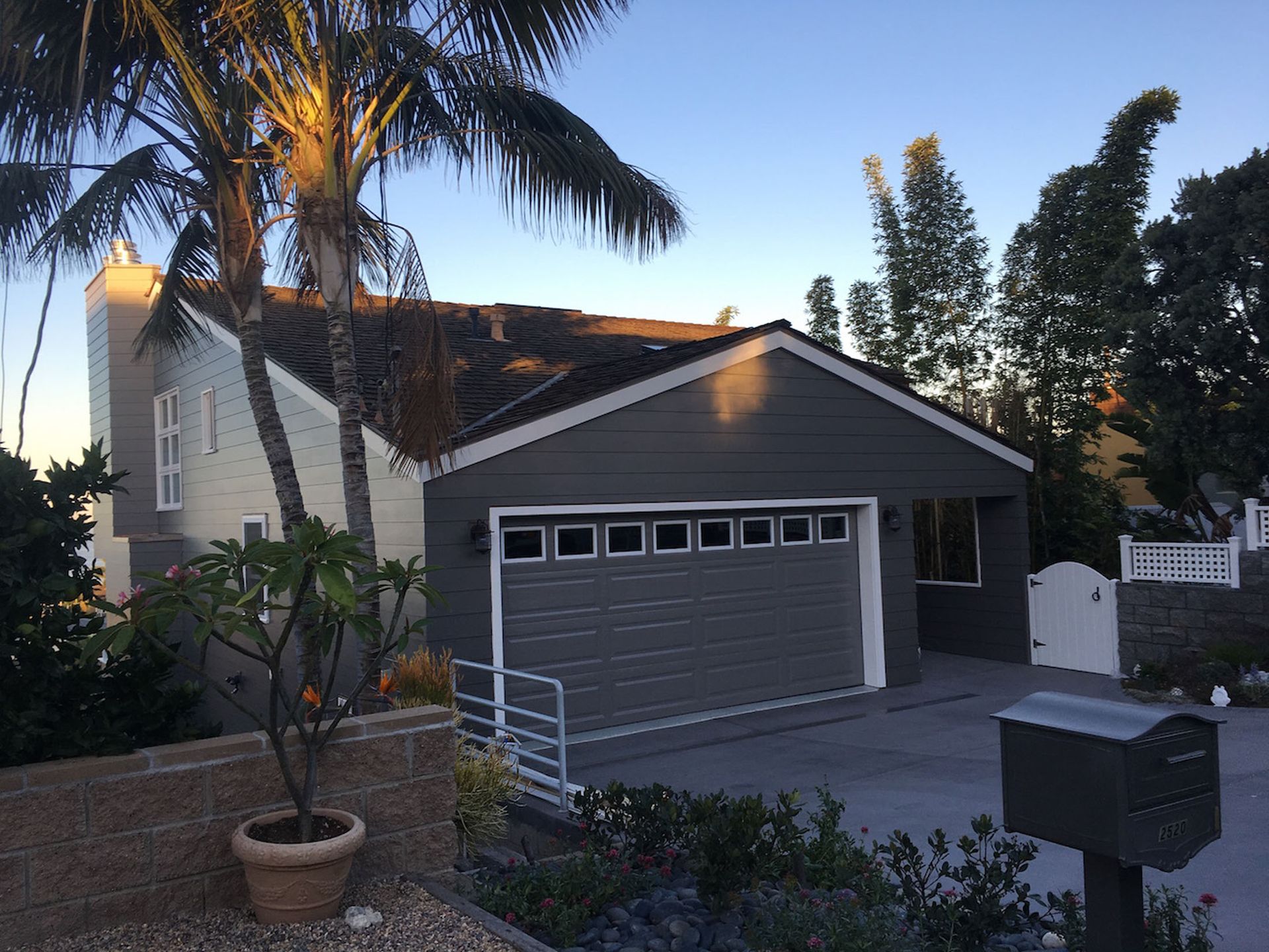 A house with a gray garage door, palm tree, and a driveway at dusk.