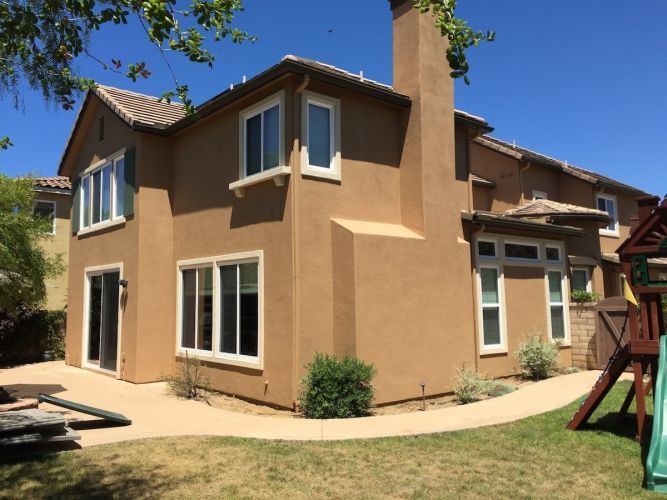 Tan two-story house with white window frames and a chimney.  A concrete patio and green lawn. Blue sky.