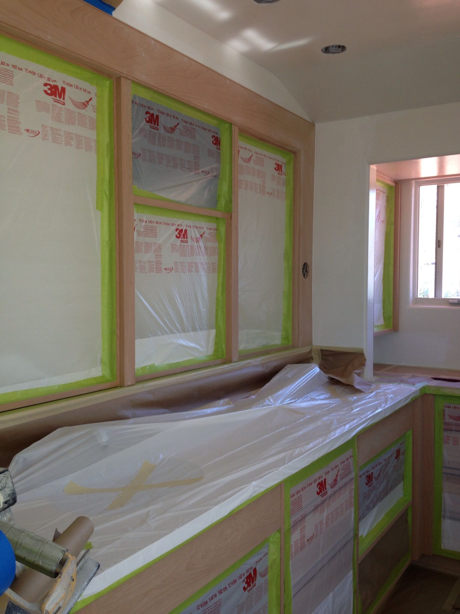 Kitchen cabinets and windows covered with plastic and tape, ready for painting.