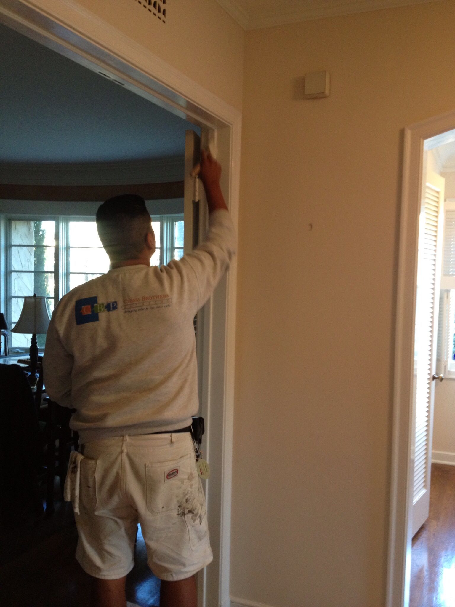 Painter in white clothes, painting a door frame in a hallway.