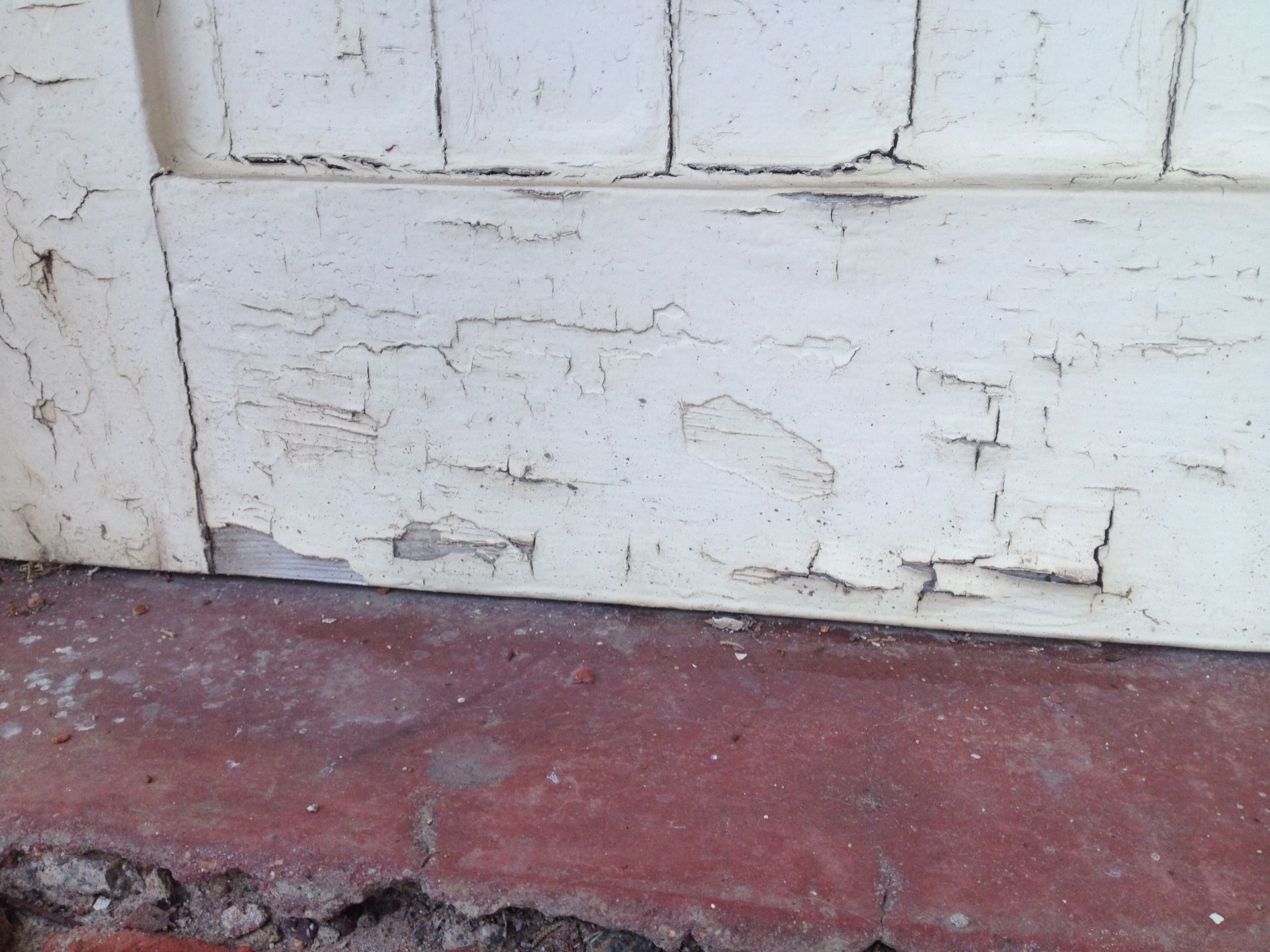 Flaking white paint on a wooden door panel above a cracked red concrete floor.