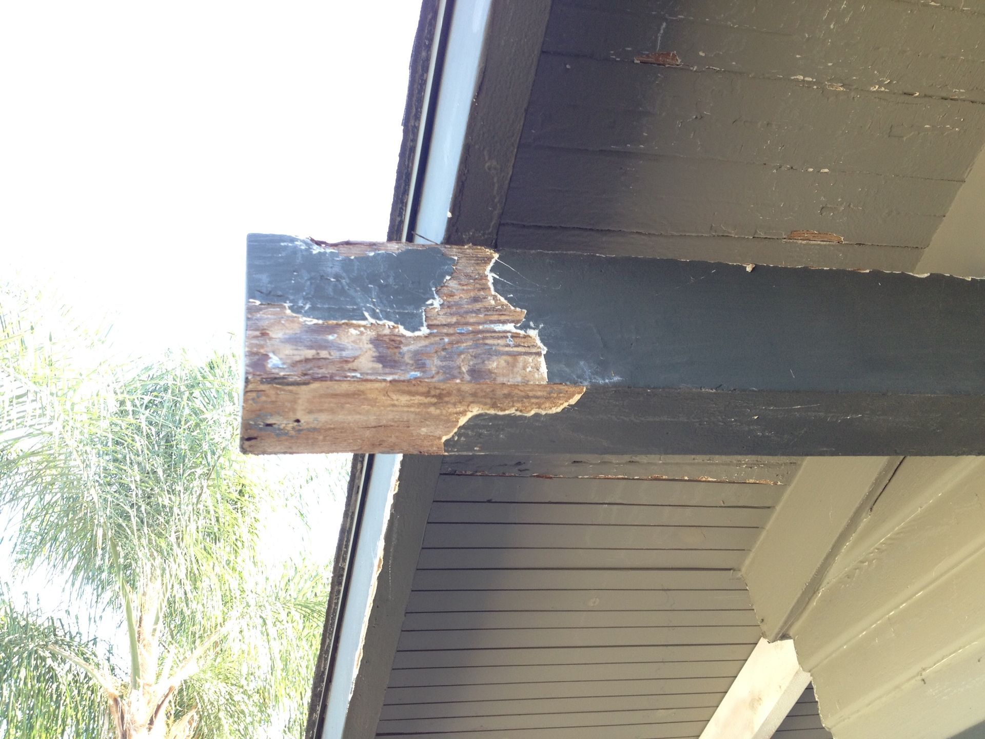 Damaged wooden beam on a house, with paint peeling off, revealing deteriorated wood.