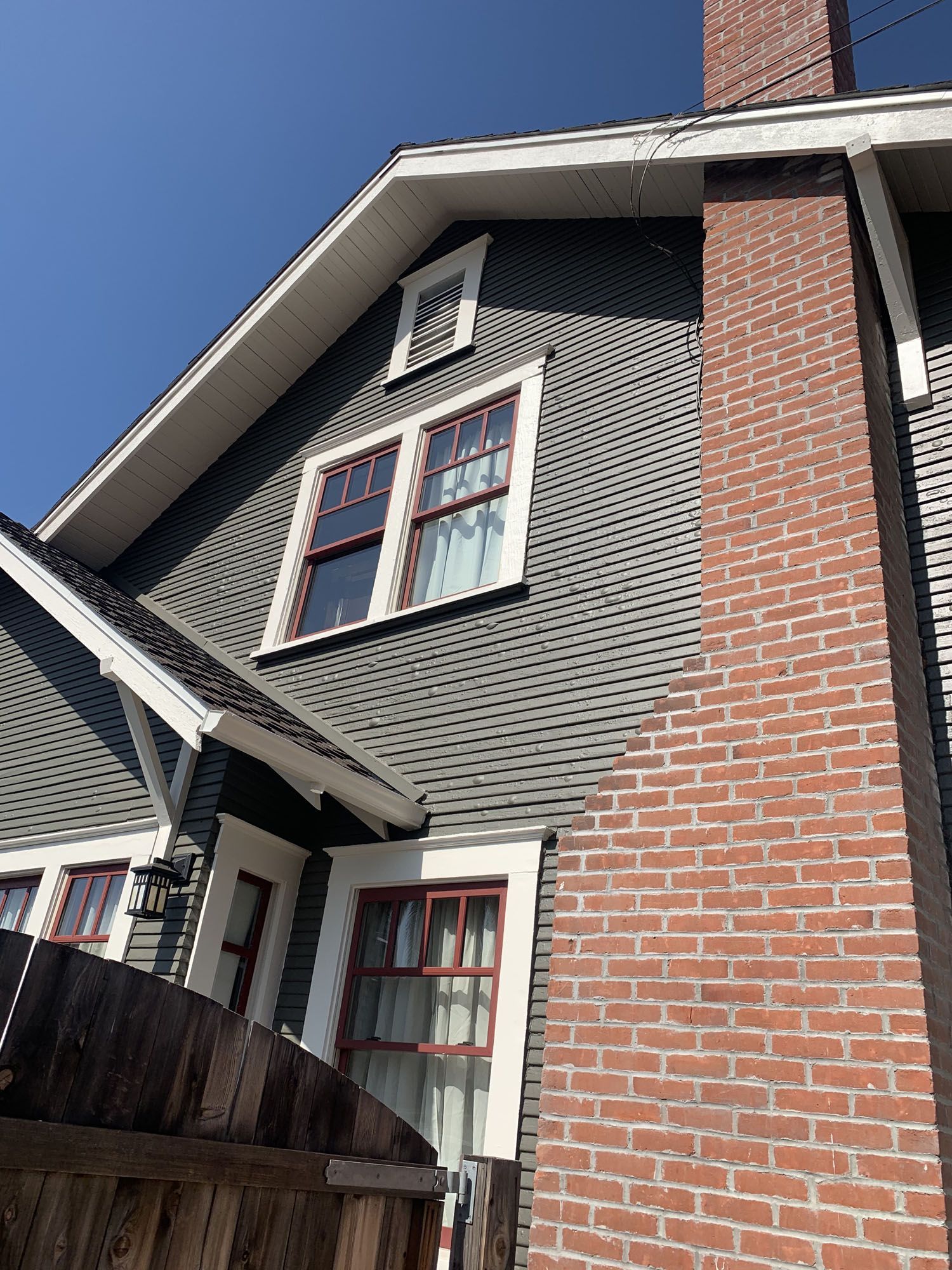 Gray-sided house with white trim and a red brick chimney under a blue sky.
