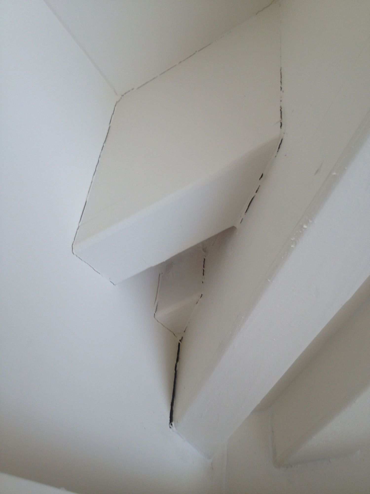 White painted wood beams meeting at an inside corner, showing dark lines along the joins.