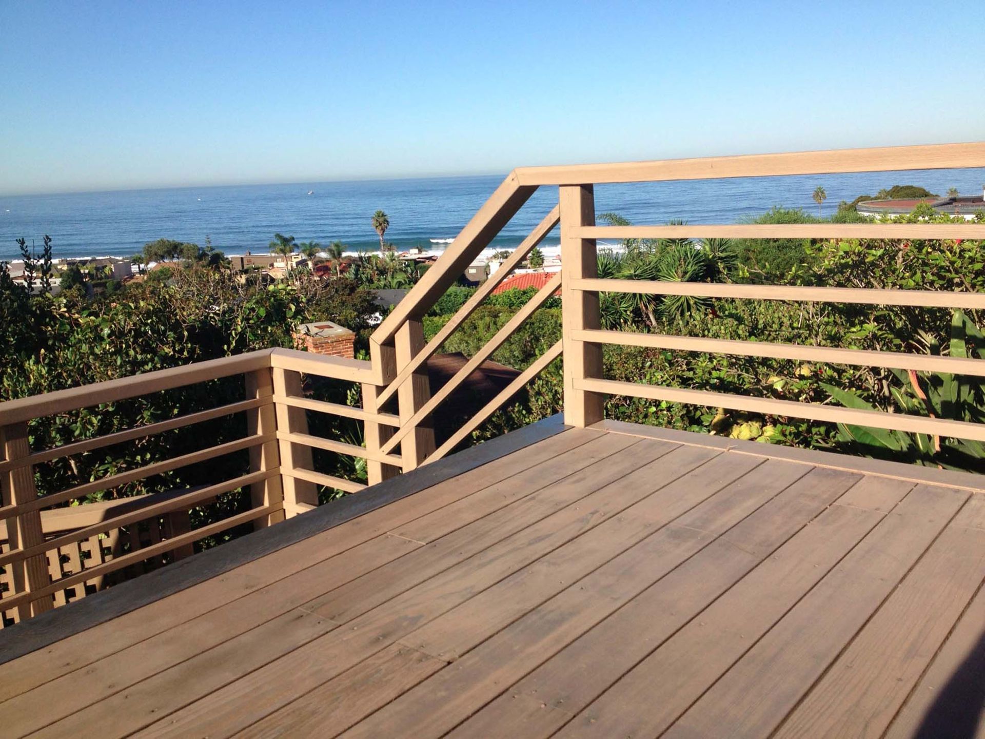 Wooden deck with railing overlooking the ocean and coastal homes on a sunny day.