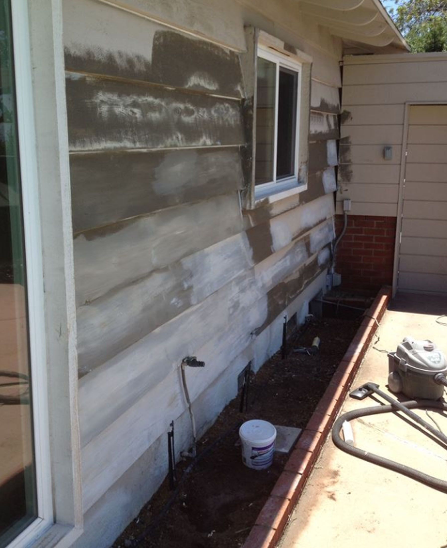 House exterior with exposed siding and applied stucco. Brick planter and window visible.