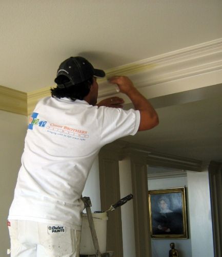 Person painting crown molding on a ceiling from a step ladder.