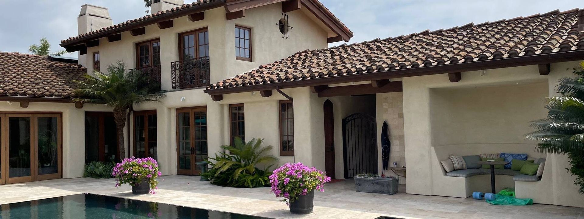 Exterior view of a stucco house with a tile roof and a swimming pool.