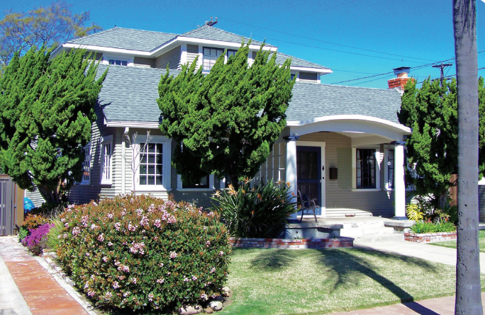 Tan house with green roof and landscaping, sunny day.