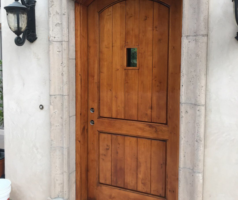Wooden door with a small window, set in a stone frame, flanked by sconce lights.