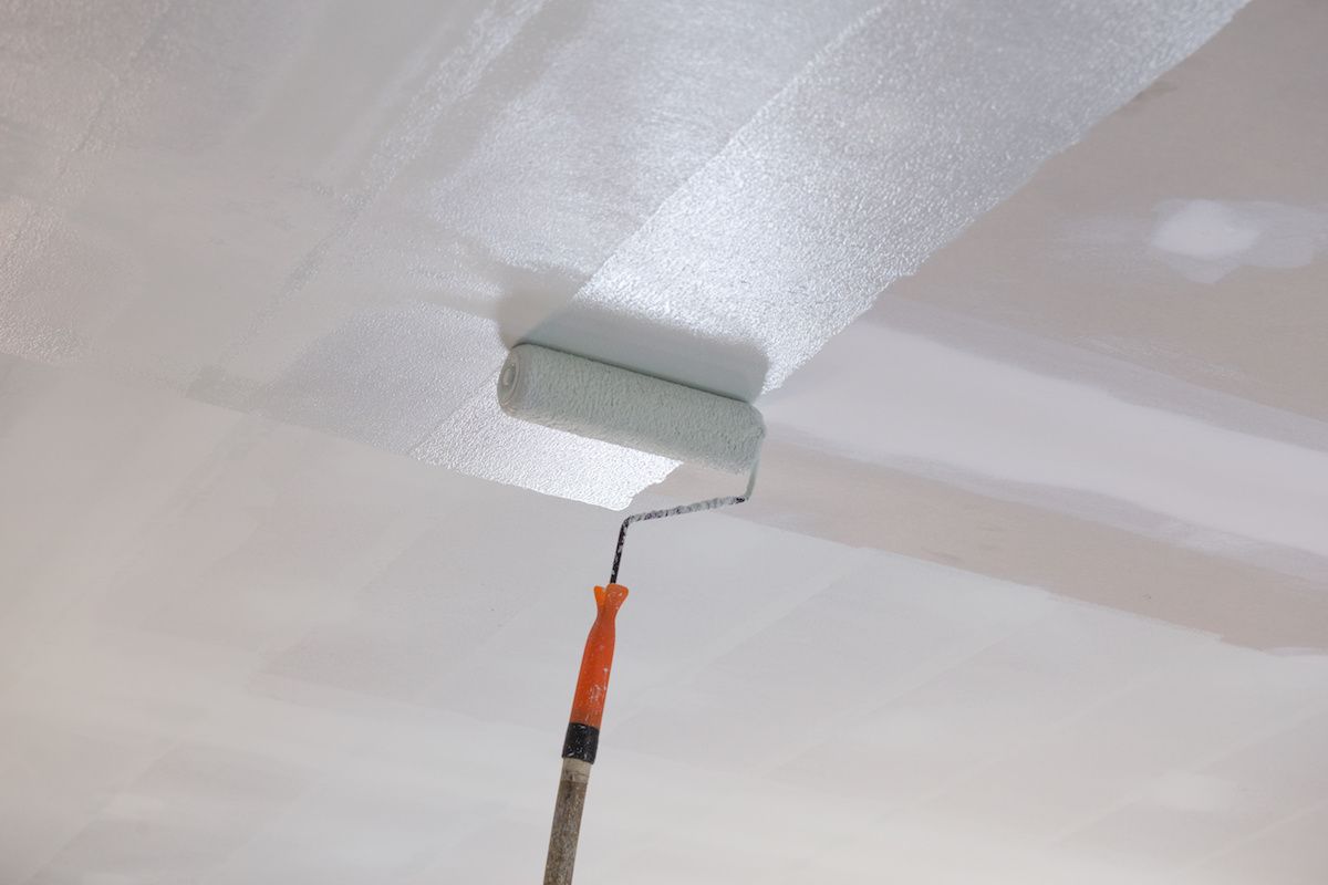 A paint roller applies white paint to a ceiling, leaving a textured strip.
