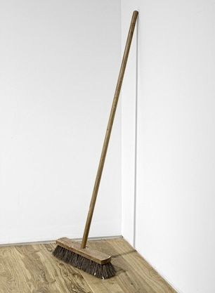 Broom leaning against white walls in a corner, placed on wooden floor.