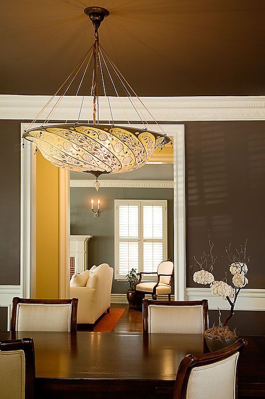 Dining room with dark brown walls, white trim, and a large chandelier over a wooden table.