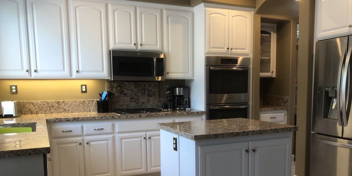 White kitchen with granite countertops, stainless steel appliances, and an island.