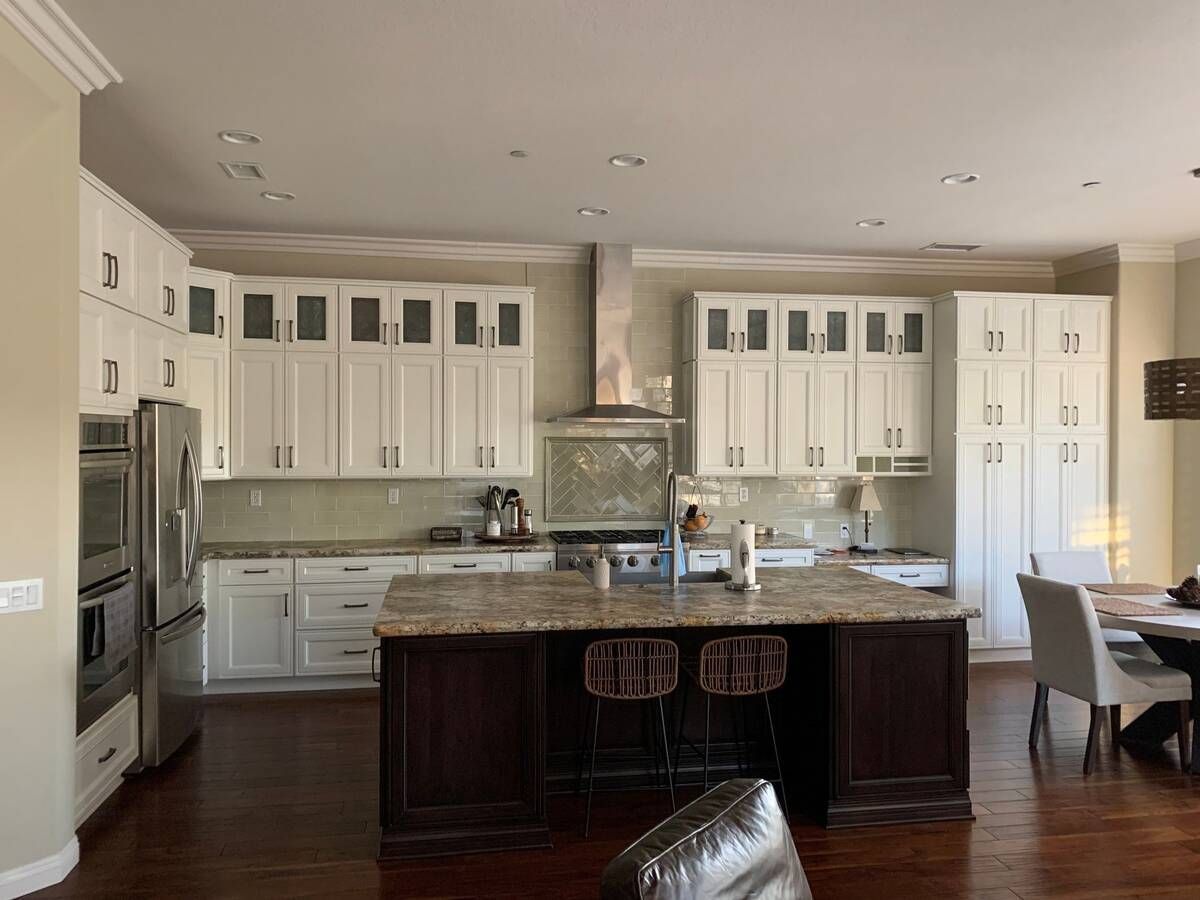 Spacious kitchen with white cabinets, brown island, granite countertops, stainless steel appliances, and a dining table.