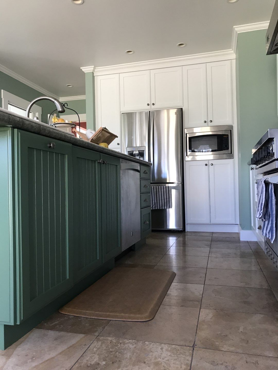 Kitchen with green island, stainless steel refrigerator, white cabinets, and tile floor.