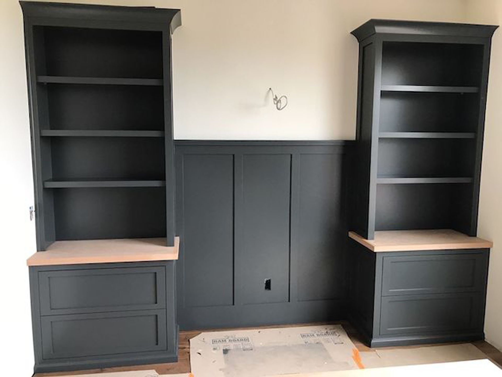 Two dark gray bookshelves with light wood tops flank a paneled wall in a room.