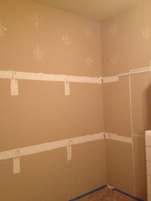 Beige walls with white shelving supports and fleur-de-lis stencil pattern. Corner of a room.