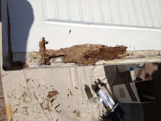 Damaged white door frame with significant wood rot at the base. Brown debris visible.