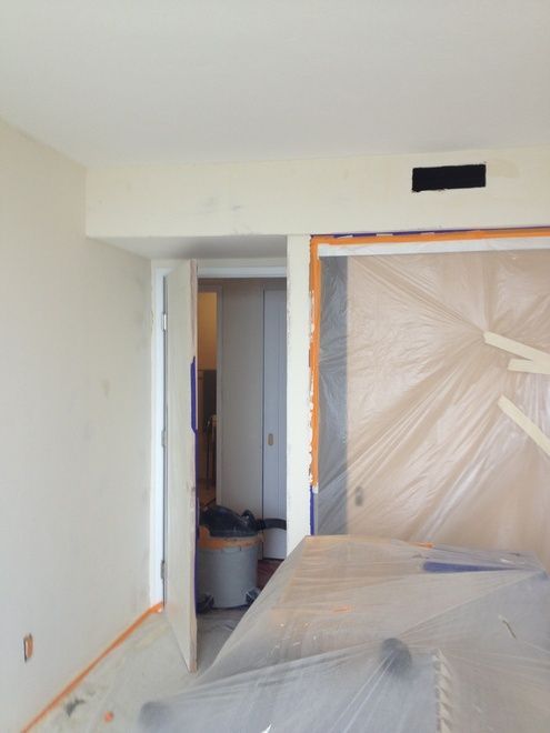 Room with open doors, plastic sheeting, and masking tape, possibly under renovation.