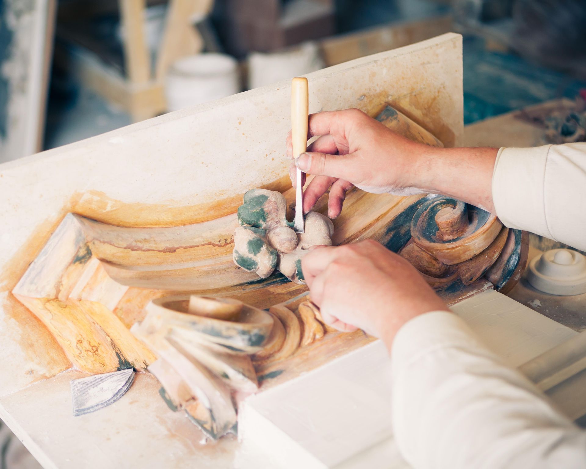 Hands carving detailed ornate stone relief with a tool, working on architectural design.