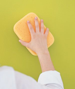 Hand using a yellow sponge to clean a green wall.