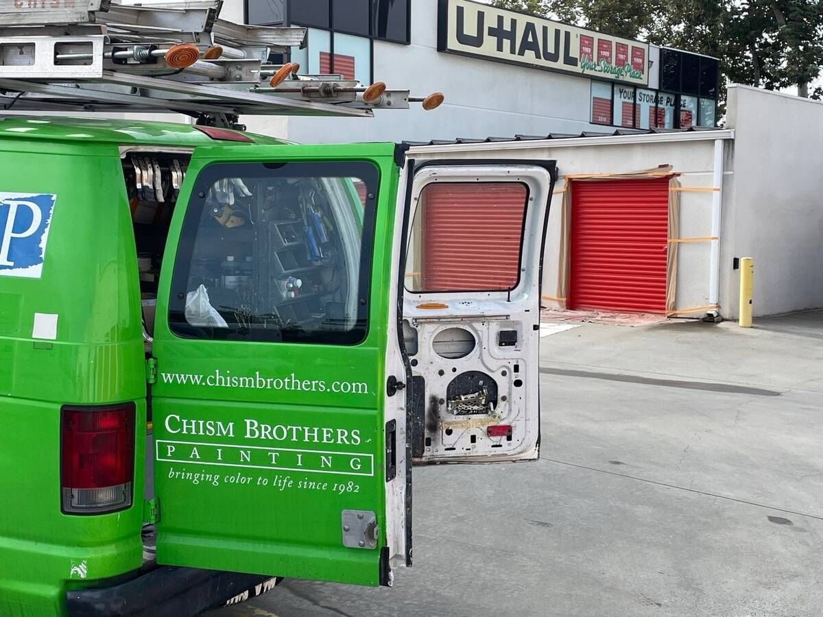 Green van with open door next to red storage units at a U-Haul facility.