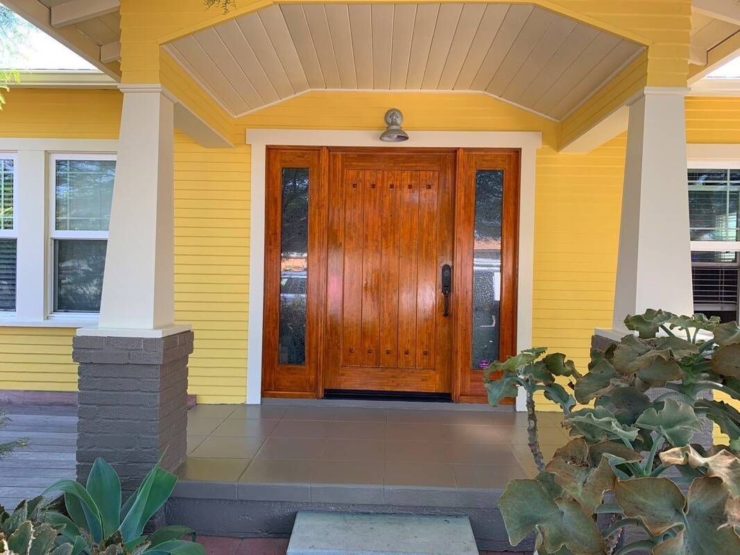 Yellow house entrance with wooden door, sidelights, and gray porch.