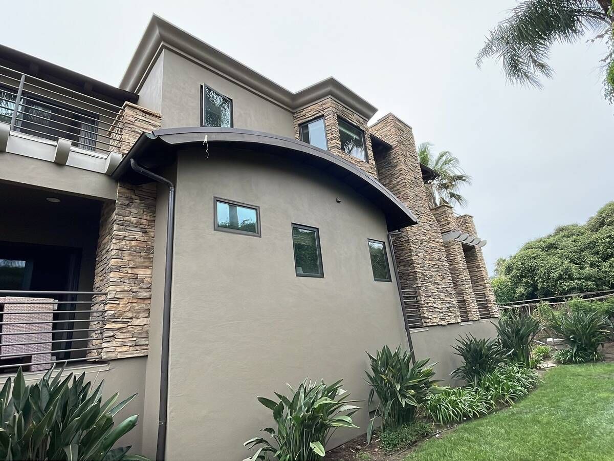 Multi-story home with stone and stucco facade, arched roof, and green landscaping.