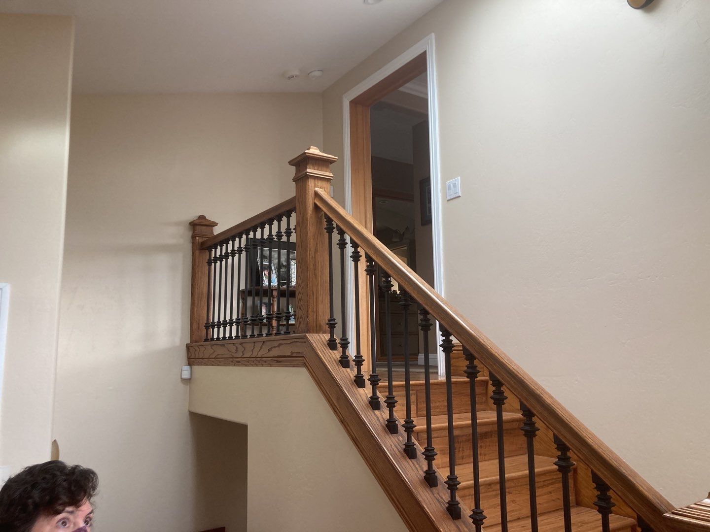 Staircase with wooden railing and black iron balusters, leading up to a doorway and second floor. Beige walls.
