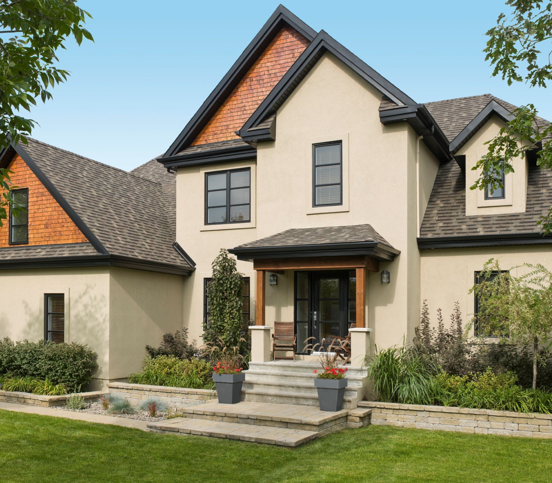 Beige stucco house with dark trim, red brick accents, and a front porch.
