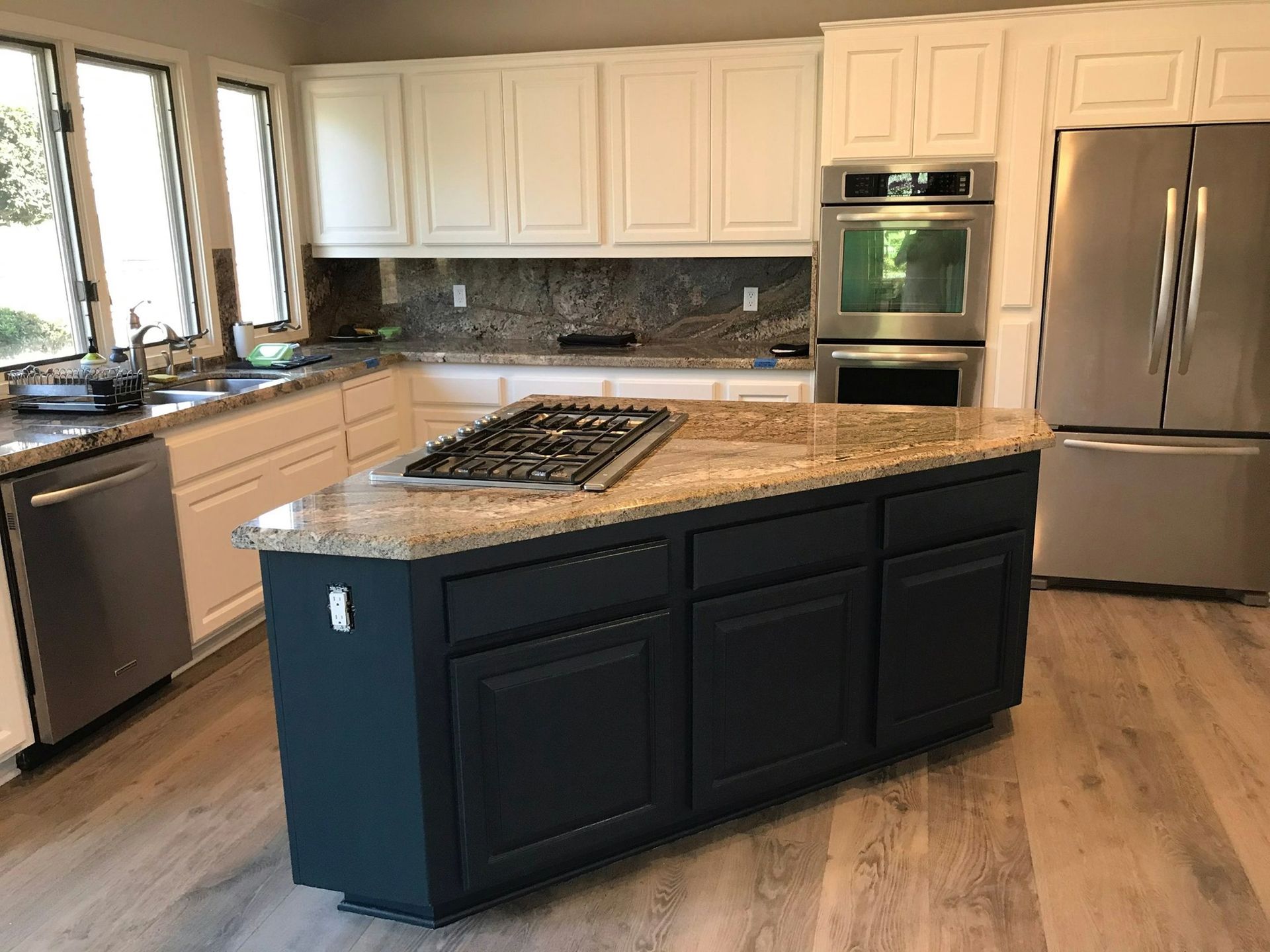 Kitchen with white upper cabinets and a dark blue island with a stovetop.
