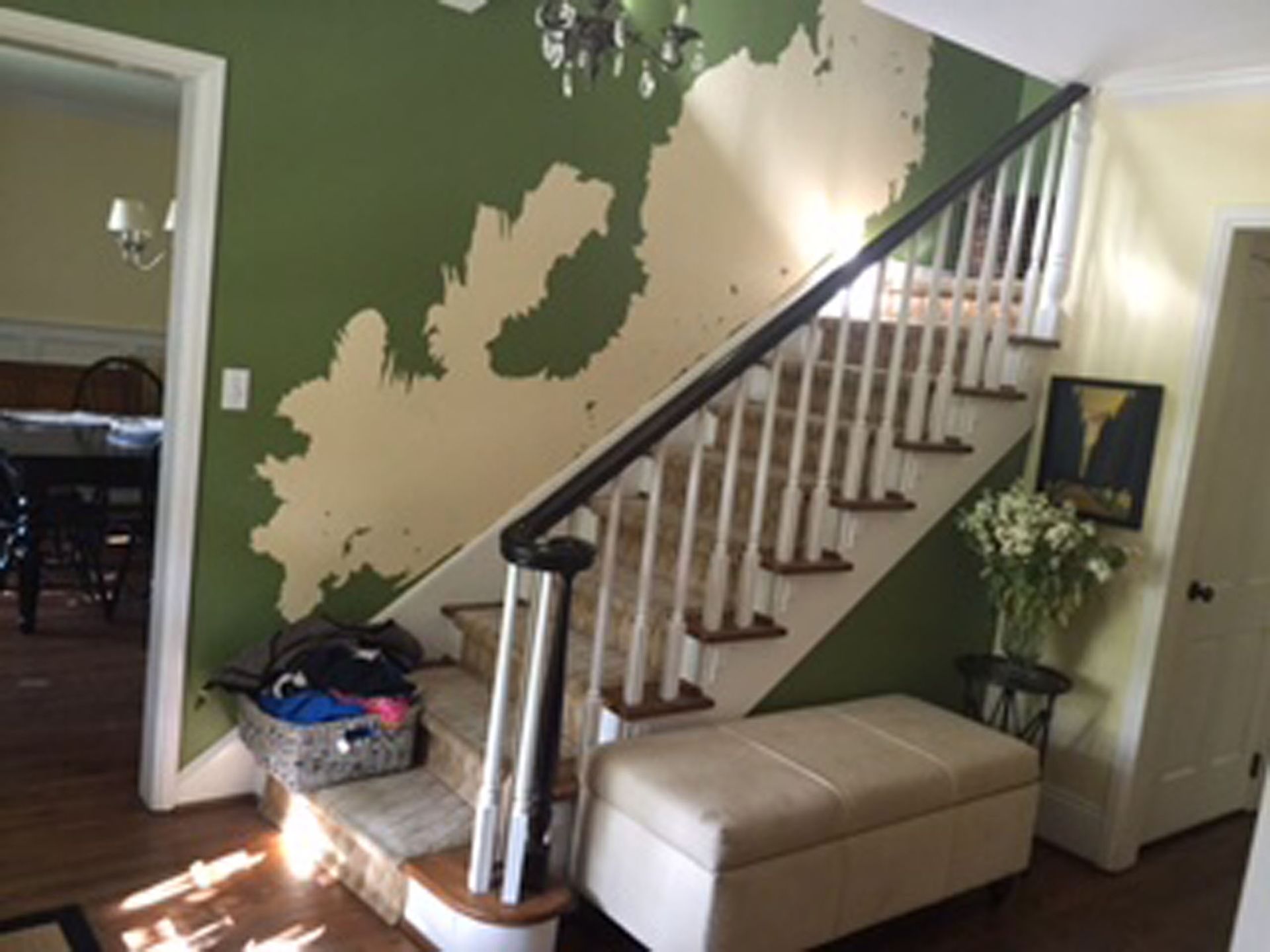 Green wall with a beige splotch, a staircase, and an upholstered bench at the bottom.