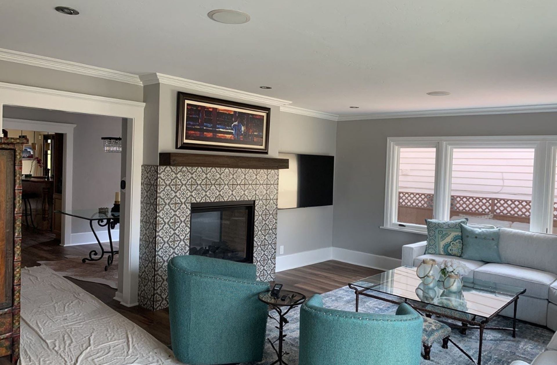 Living room with fireplace, teal chairs, and a window. Gray walls and white trim.