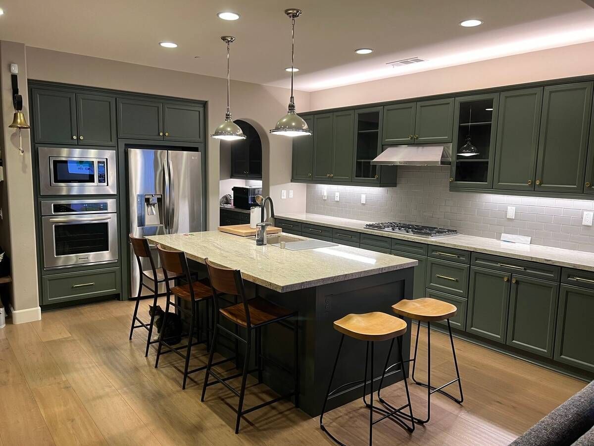 Green kitchen with island, stainless steel appliances, and wood floors.
